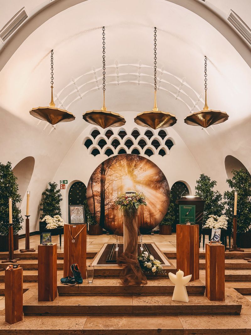 Innenraum einer modernen Kirche mit dekorativer Beleuchtung, einem runden Kunstwerk hinter dem Altar und Blumenschmuck.
